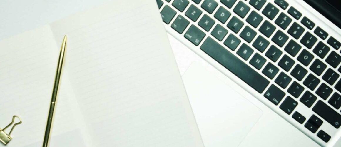 Notebook with a golden pen on top of a laptop keyboard.